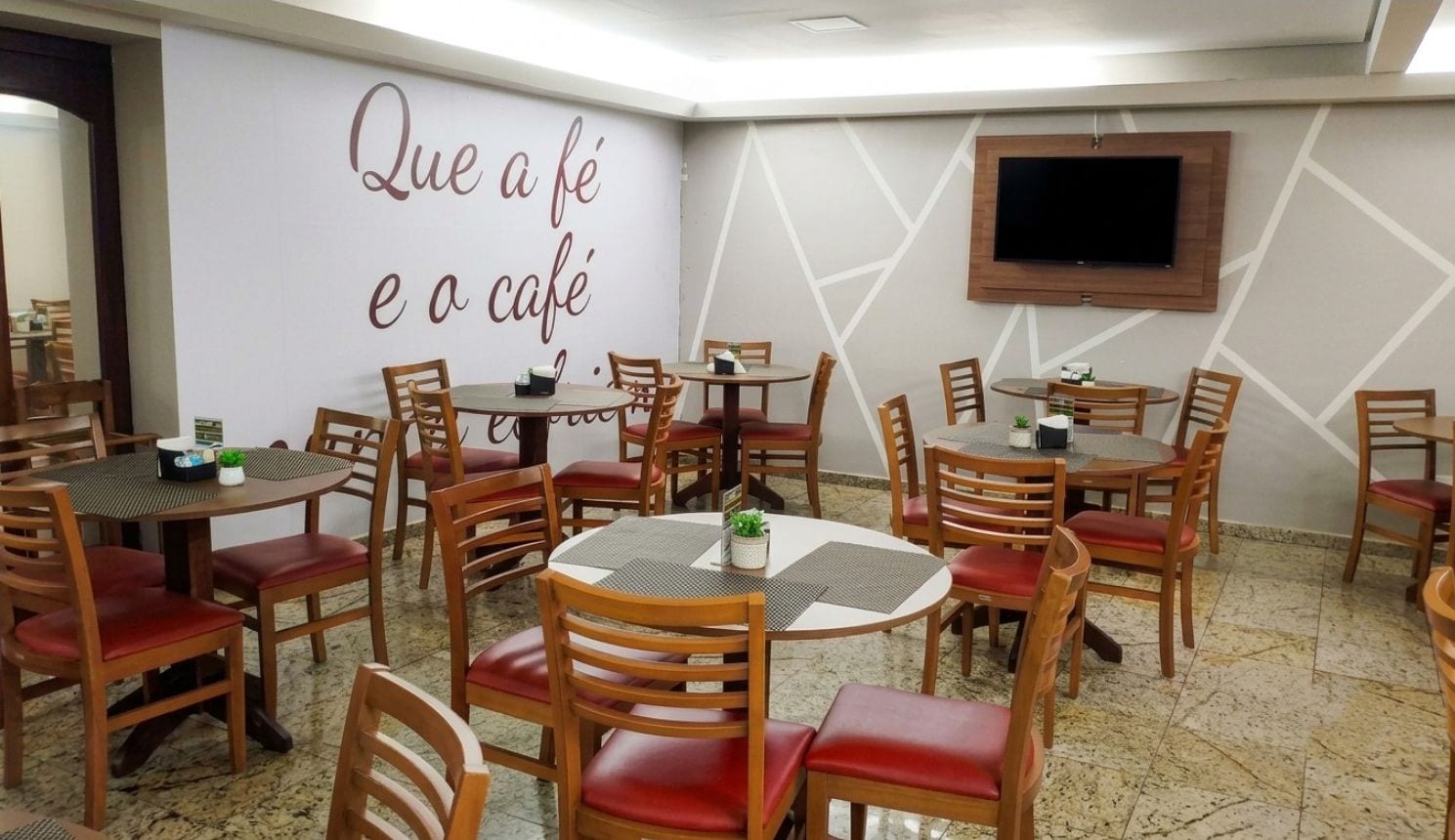 Un café avec plusieurs tables et chaises, un mur orné d’une citation inspirante et un téléviseur fixé au mur.