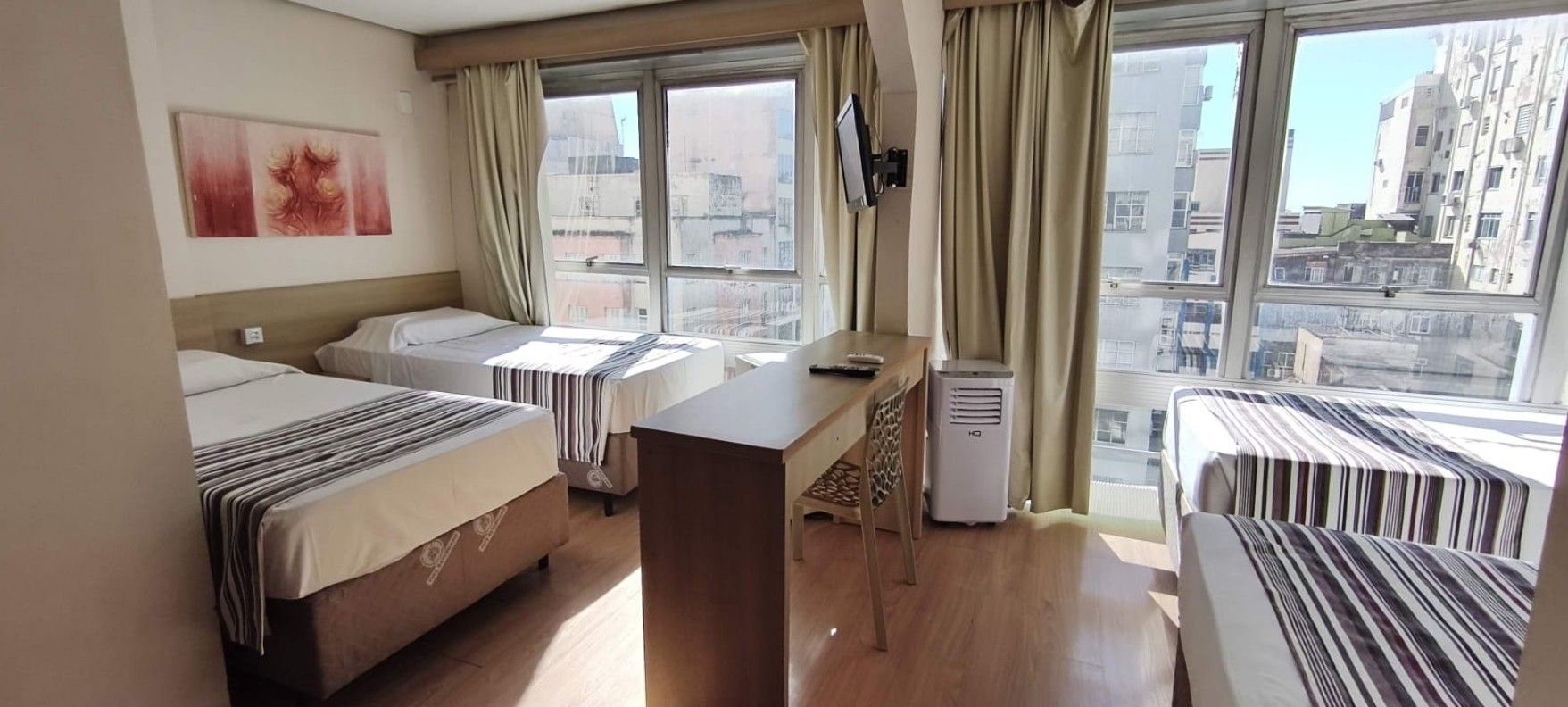 A hotel room with two beds, a desk, a chair, a TV, and a window with a city view.