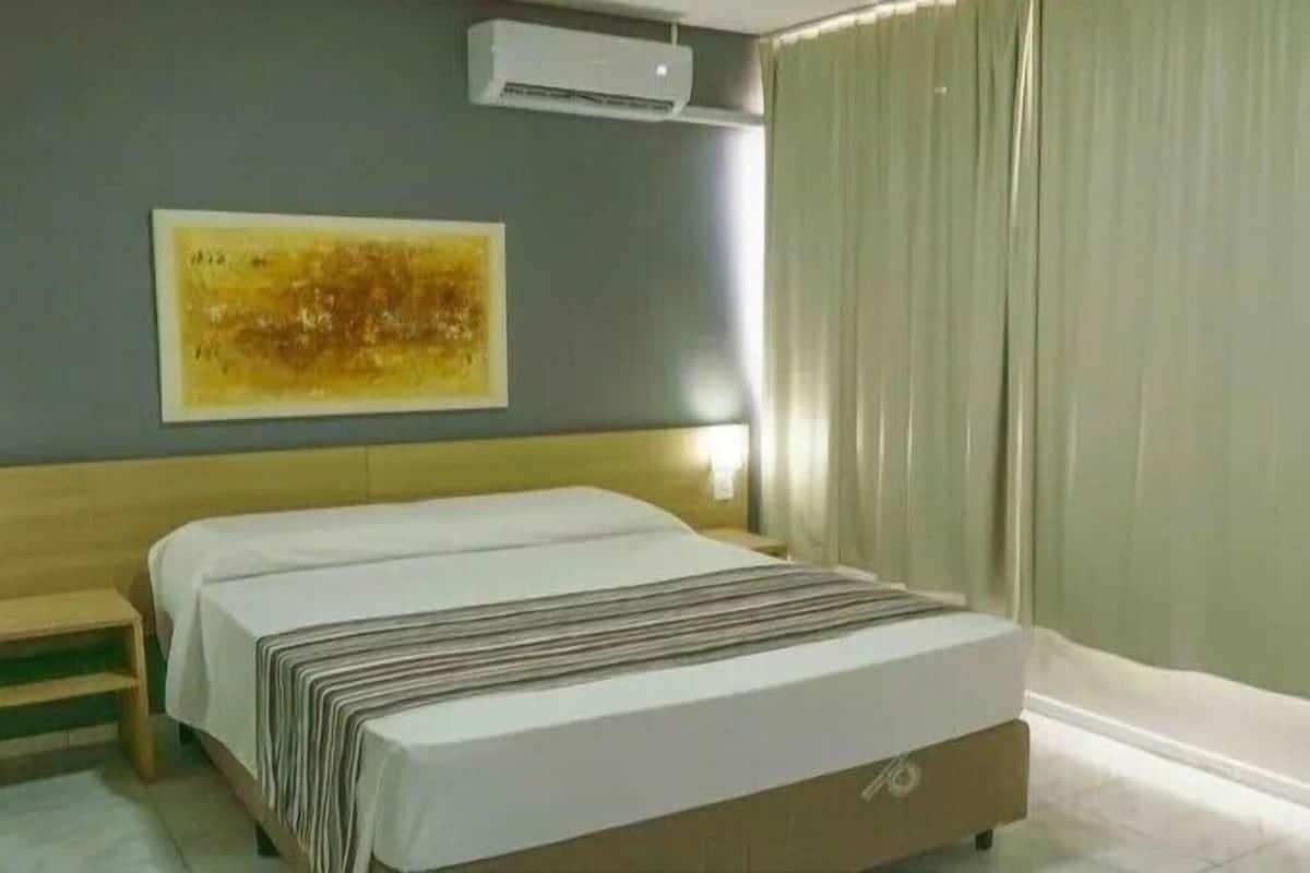 Quarto de hotel com cama, mesa de cabeceira, ar condicionado fixado na parede e um quadro.