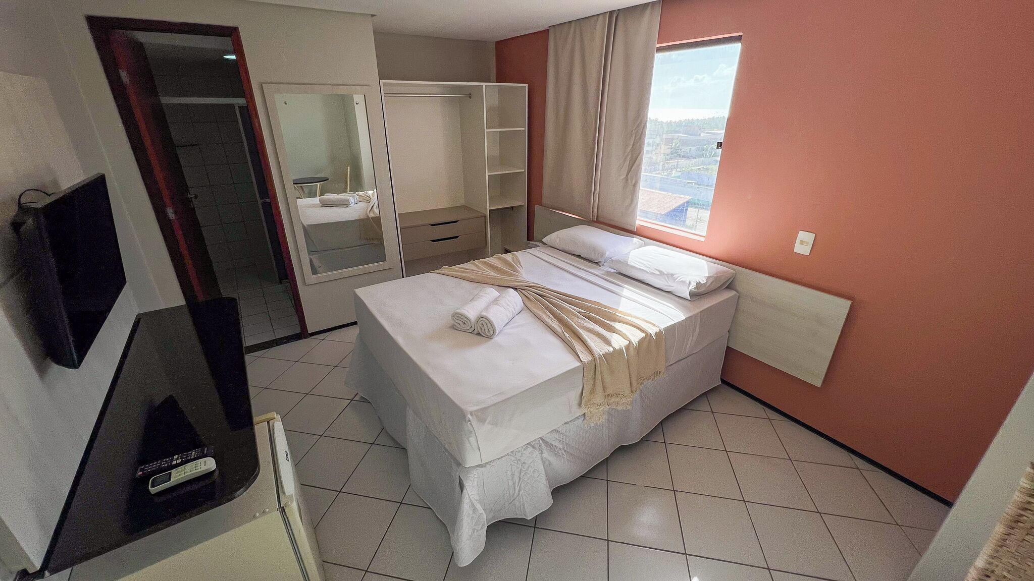 A hotel room with a bed, a TV, a wardrobe, and a window with a view.