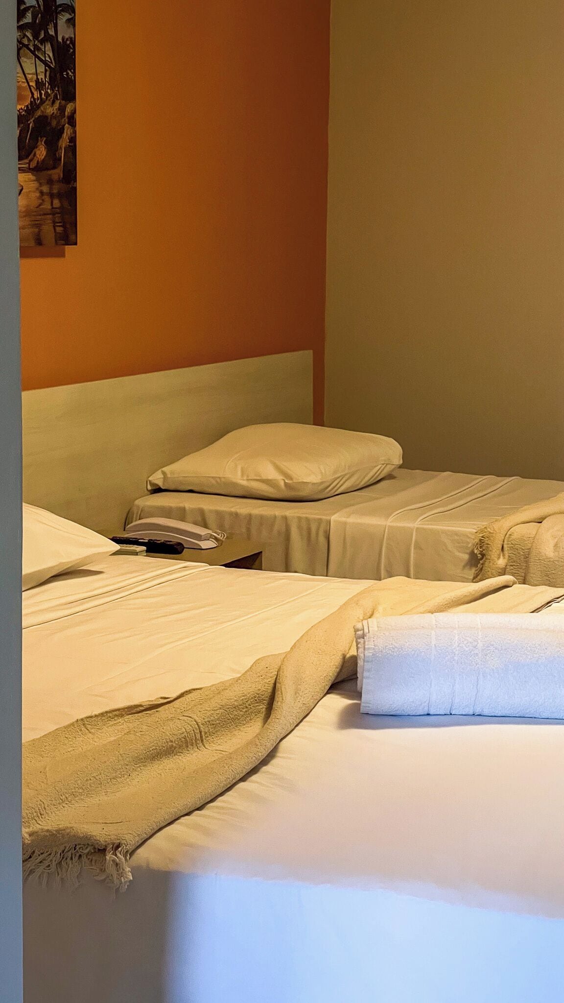 A hotel room with two beds, each with white bedding and pillows. There is a telephone on the left bed, and a folded towel on the right bed.