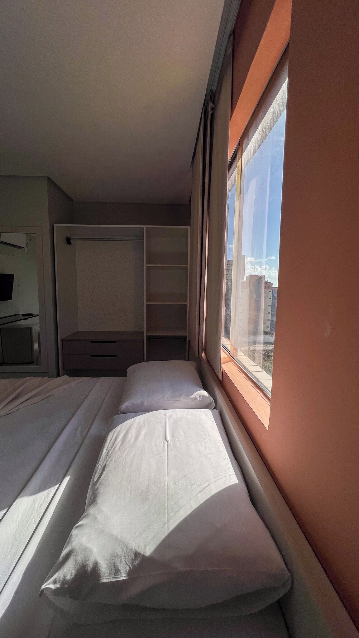 A room with two beds, a wardrobe, and a window with a city view.