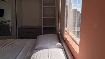 A room with two beds, a wardrobe, and a window with a city view.