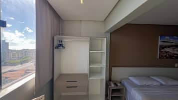 Habitació d'hotel amb una finestra gran, un armari amb espai per penjar roba, un llit i una taula de nit amb un telèfon i un comandament a distància.