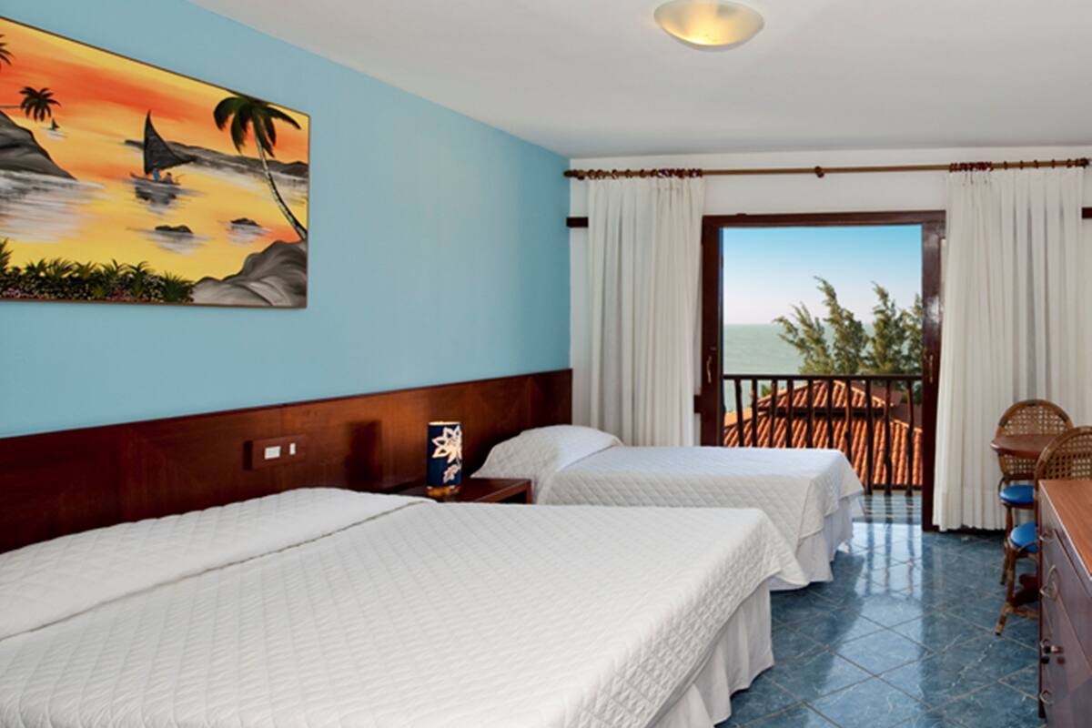 A hotel room with two beds, a painting of a sunset, a balcony with a view, and a wooden headboard.