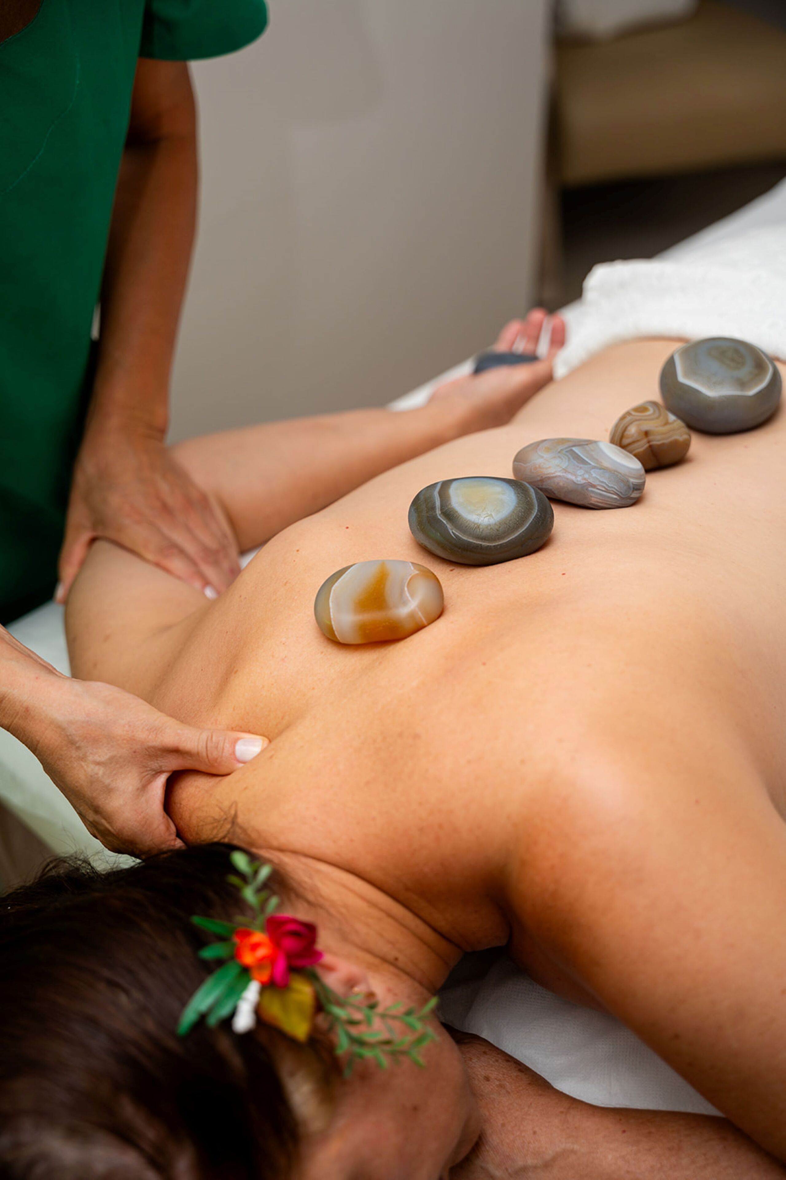 A person receiving a back massage with stones placed on their back.