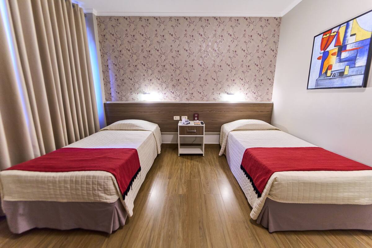 A hotel room with two beds, a nightstand, and a floral wallpaper.