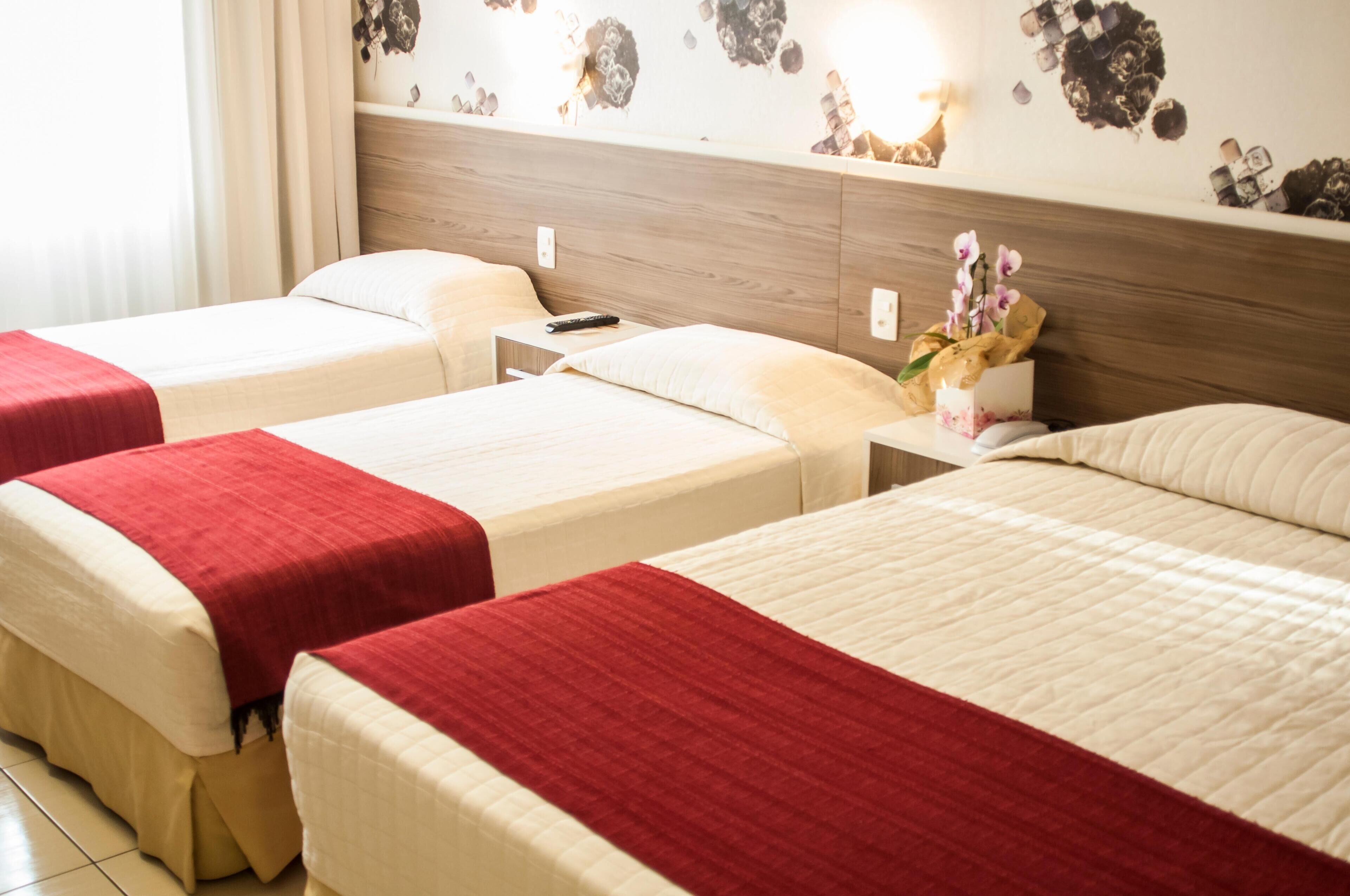 A hotel room with two beds, each with a red and white bedspread, a nightstand with a remote control, and a wall decoration.