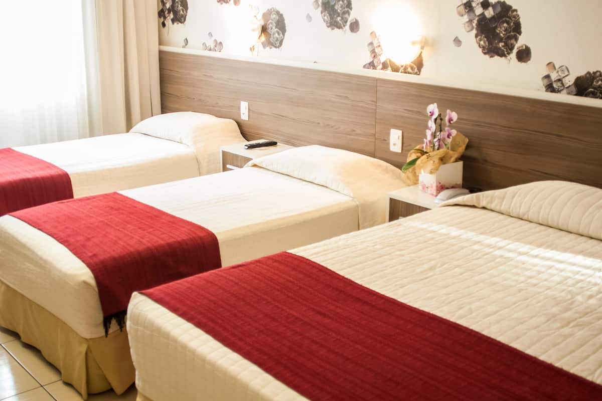 A hotel room with two beds, each with a red and white bedspread, a nightstand with a remote control, and a wall decoration.
