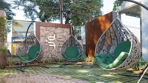 A patio area with two green cushioned hanging chairs, a stone wall with a logo, and a wooden fence. - Foz Plaza Hotel (Foz do Iguaçu)