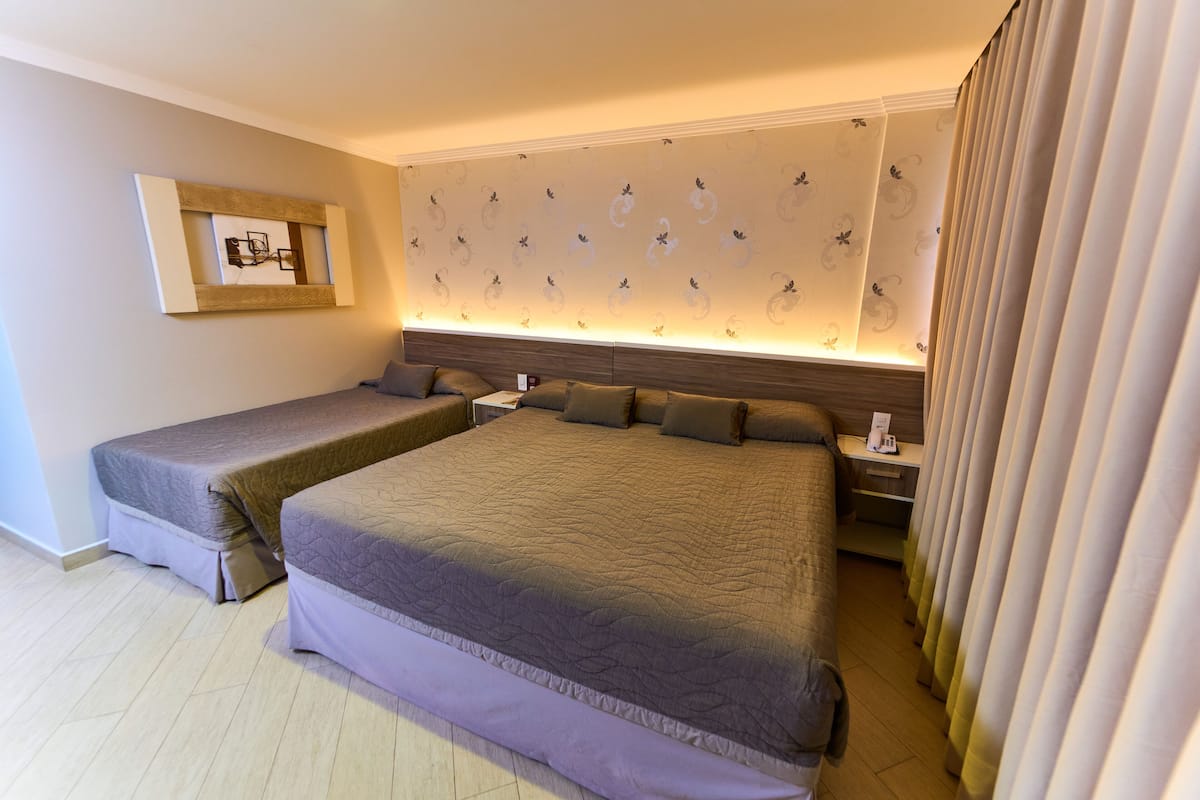 A hotel room with two beds, a nightstand, a wall-mounted artwork, and a patterned wallpaper.