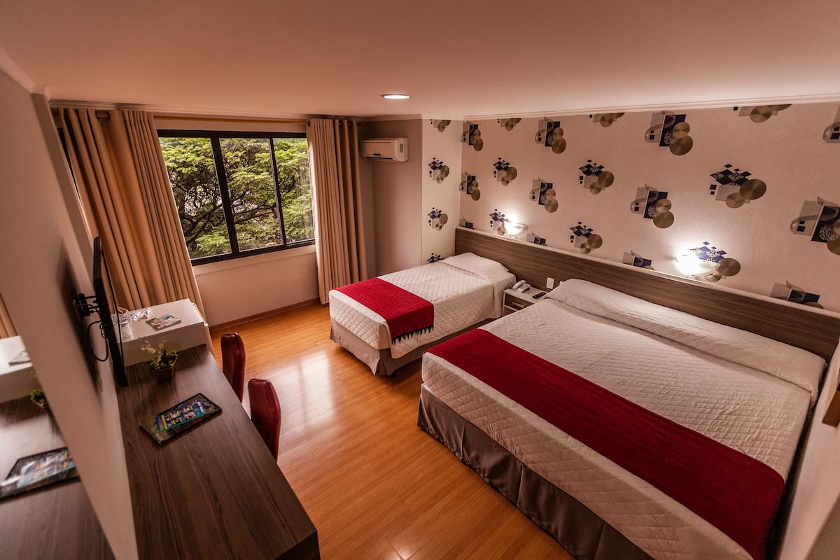 A hotel room with two beds, a desk, and a window with curtains.