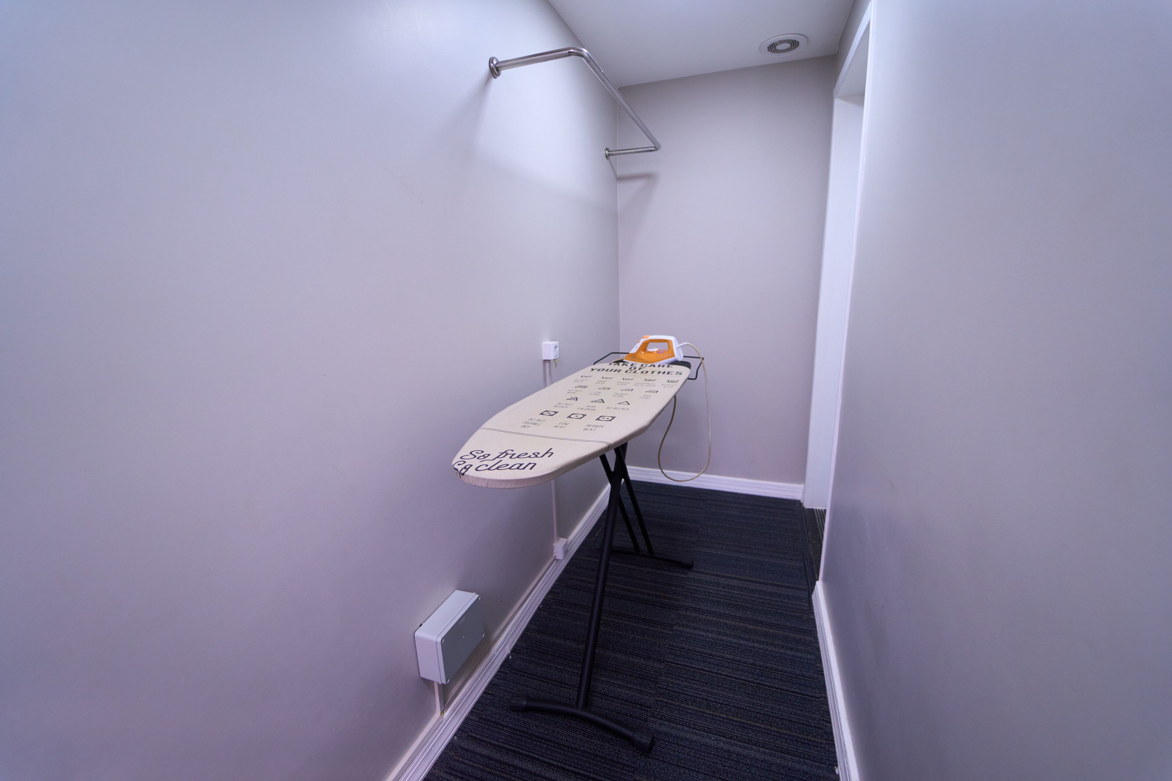 A narrow hallway with a wall-mounted ironing board and a towel rack.