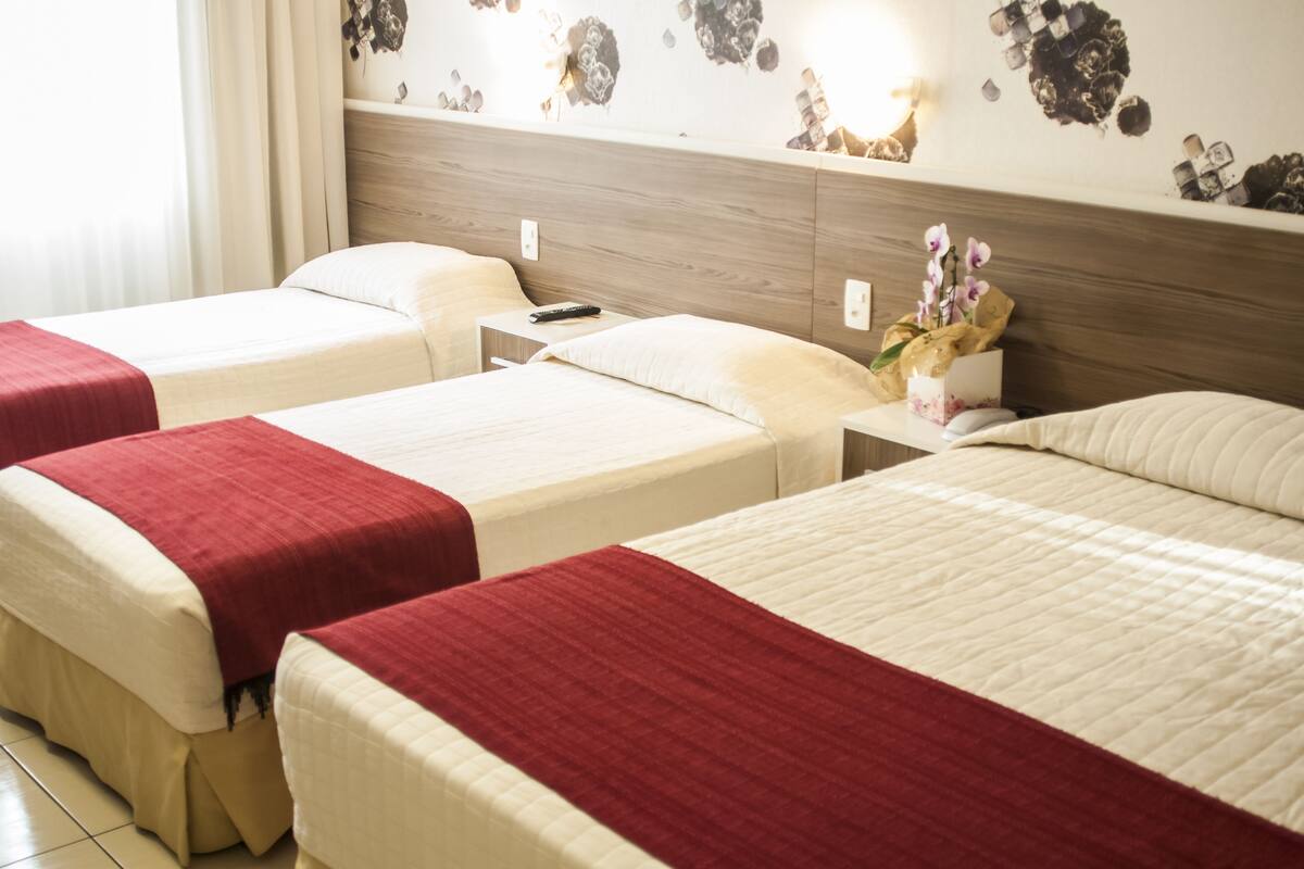 A hotel room with two beds, each with a red and white bedspread, a wooden headboard, and a nightstand with a remote control.