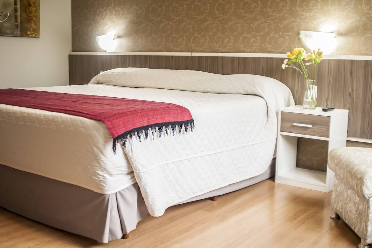A neatly made bed with a red throw, a bedside table with a vase of flowers, and a nightstand with a lamp.