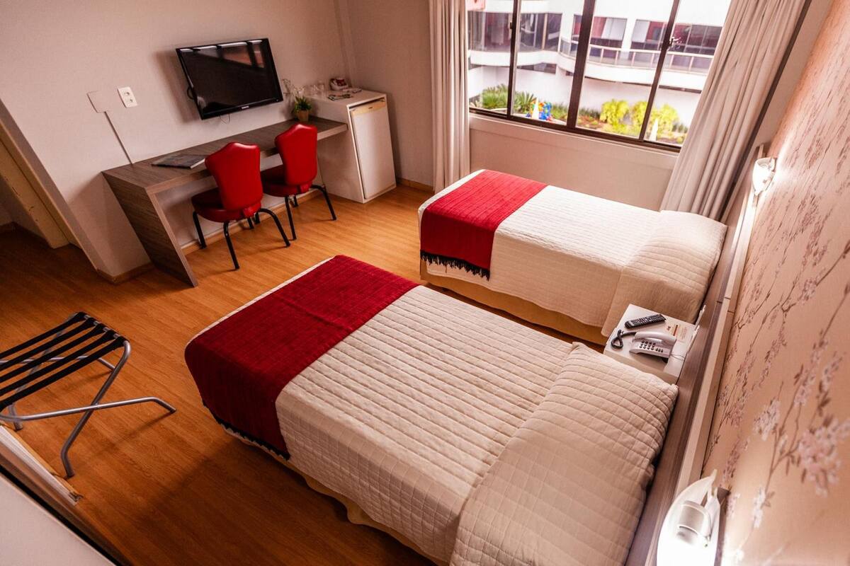 A hotel room with two beds, a desk with a chair, a TV, and a window with a view.