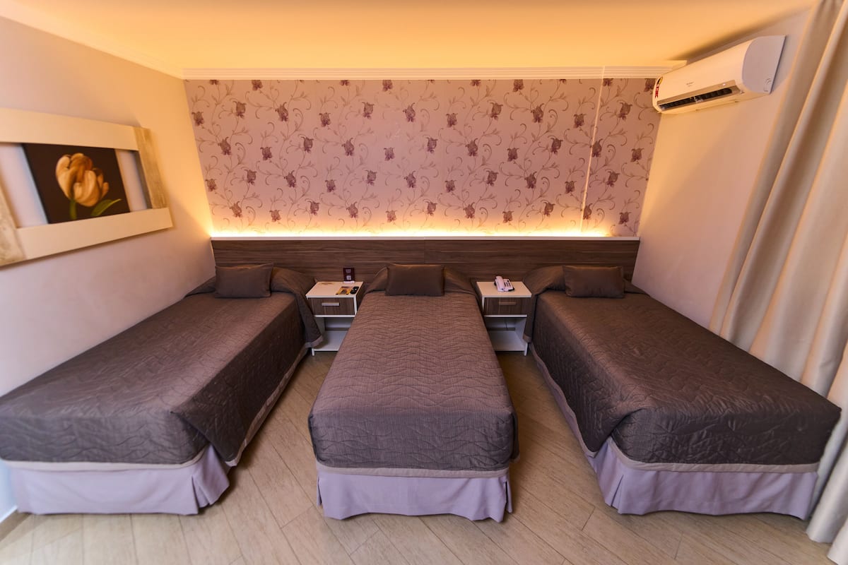 A room with three single beds, a nightstand with a lamp, and a wall-mounted air conditioner.