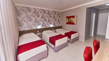 A hotel room with three beds, a dining table with red chairs, a patterned wall, and a painting on the wall.