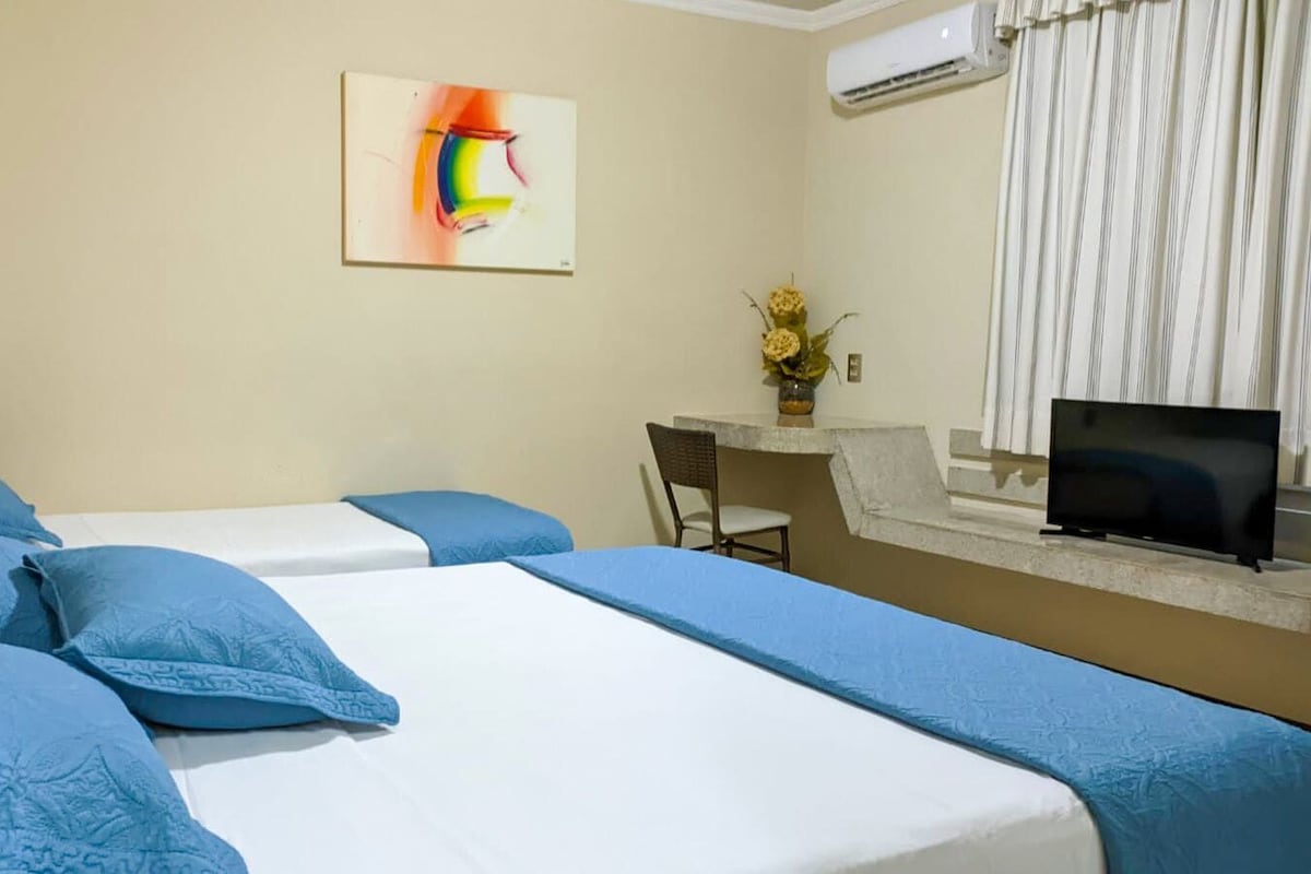 A hotel room with two beds, a desk, a chair, a television, and a painting on the wall.