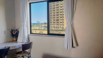 A room with a window overlooking a building and a view of the beach.