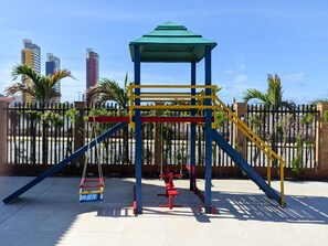 A playground with a climbing structure, swings, and a fenced area with palm trees. - Golden Beach Hotel (Fortaleza)
