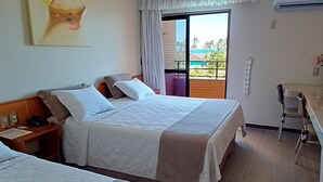 A hotel room with two beds, a desk, a chair, a window with a view, and an air conditioning unit. - Golden Beach Hotel (Fortaleza)
