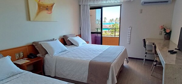 A hotel room with two beds, a desk, a chair, a window with a view, and an air conditioning unit. - Golden Beach Hotel (Fortaleza)