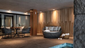 A modern indoor pool area with a seating area, including a round wicker sofa and two chairs, and a small table with a vase. - Hotel Alpestre (Gramado)