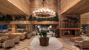 A spacious lobby with a central wooden chandelier, seating areas, a fireplace, and a view of the kitchen in the background. - Hotel Alpestre (Gramado)