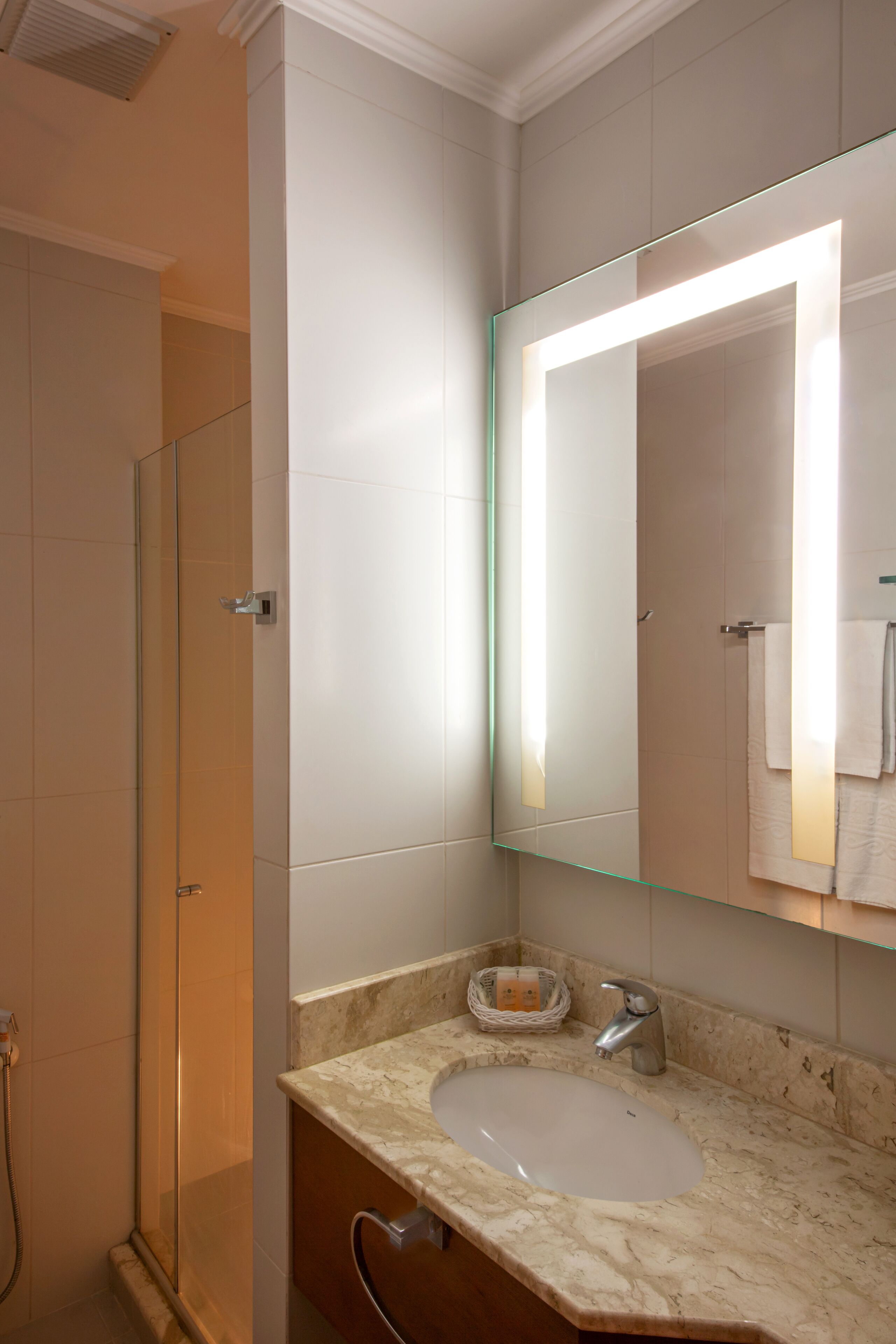 Un baño con cabina de ducha de vidrio, lavamanos de mármol y un espejo grande con iluminación integrada.
