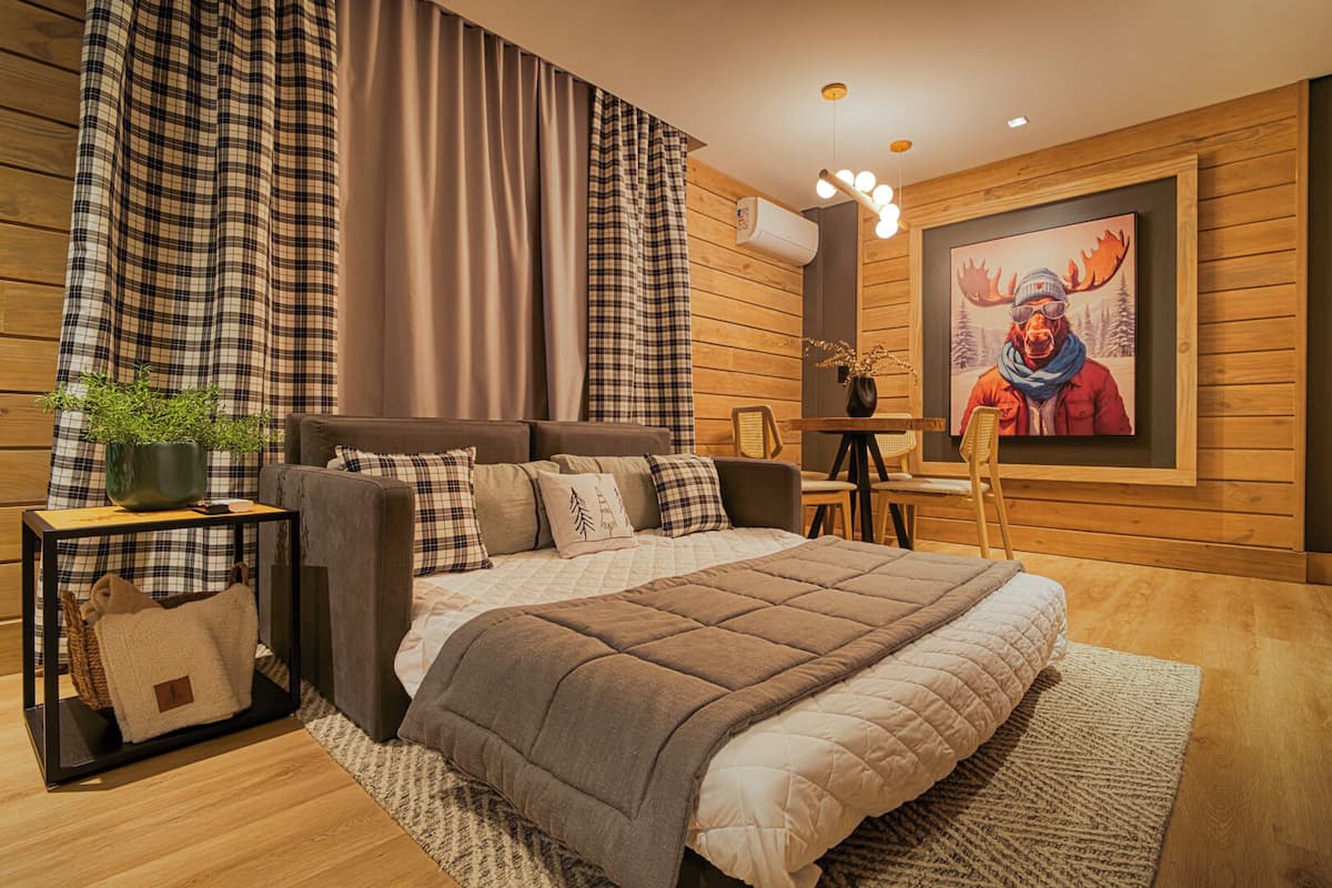 A modern bedroom with a large bed, a side table with a plant, a small table with a vase, and a painting on the wall.