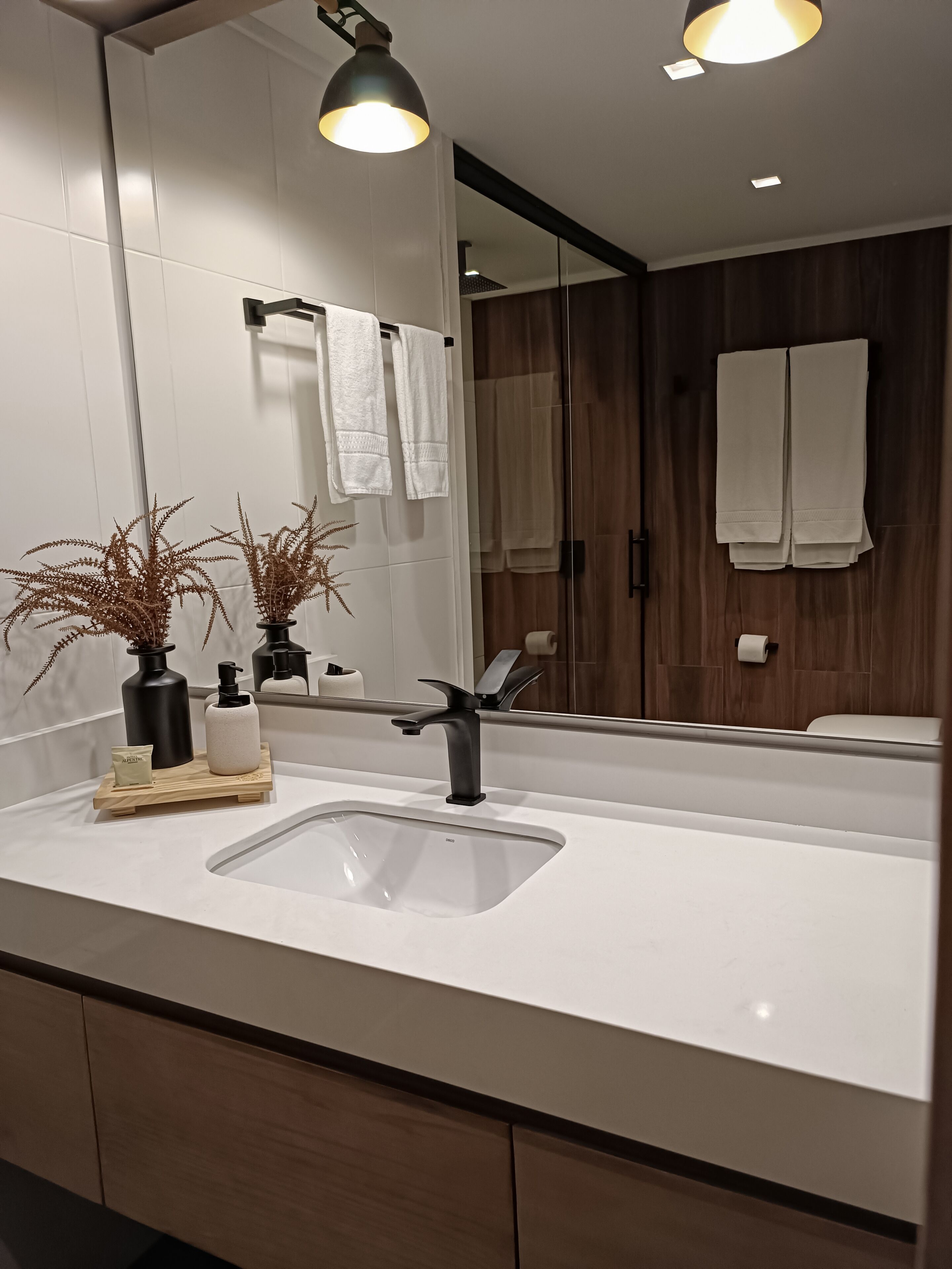 A modern bathroom with a large mirror, a sink, and two potted plants.