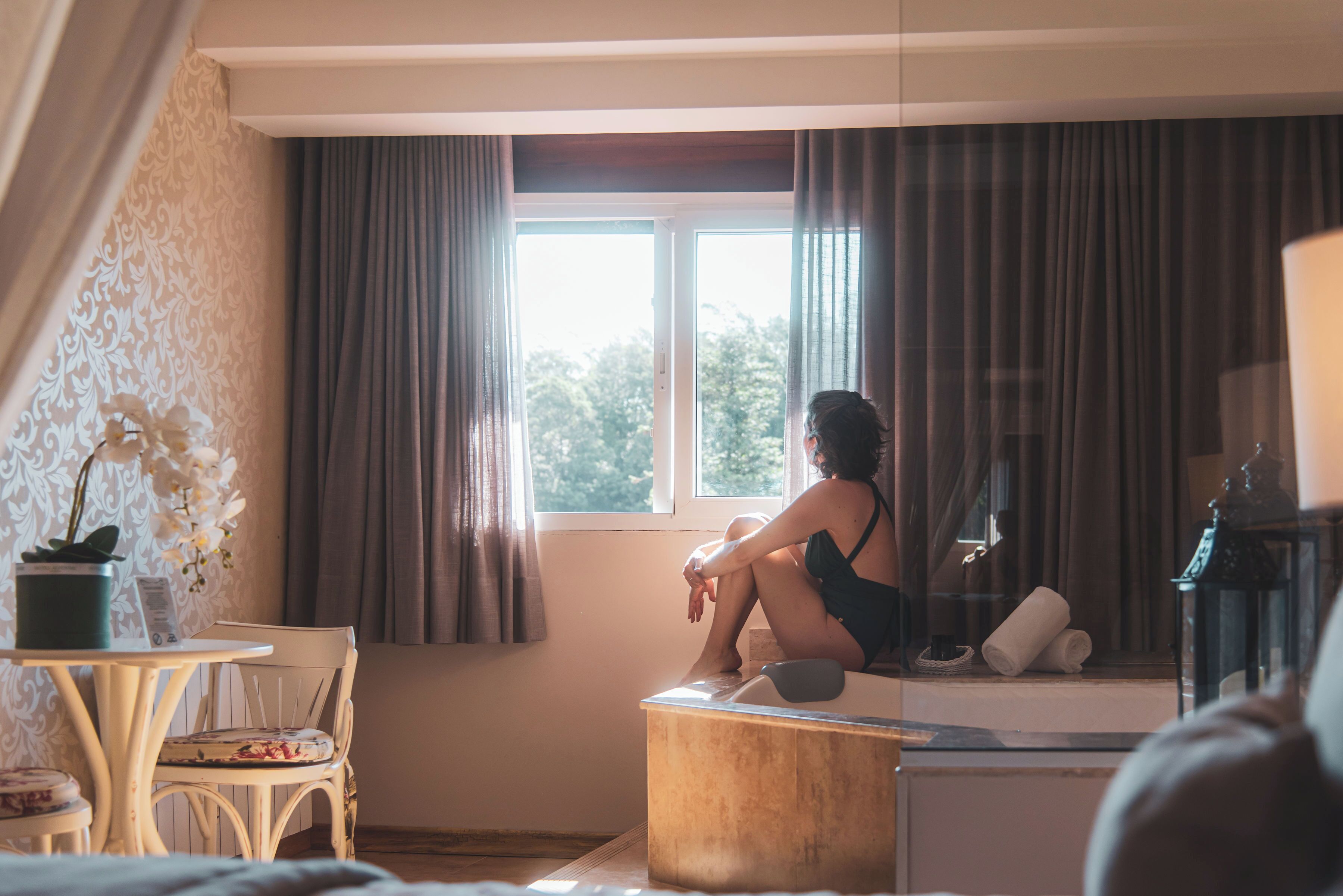 A room with a large window, a small table with a chair, and a bathtub.