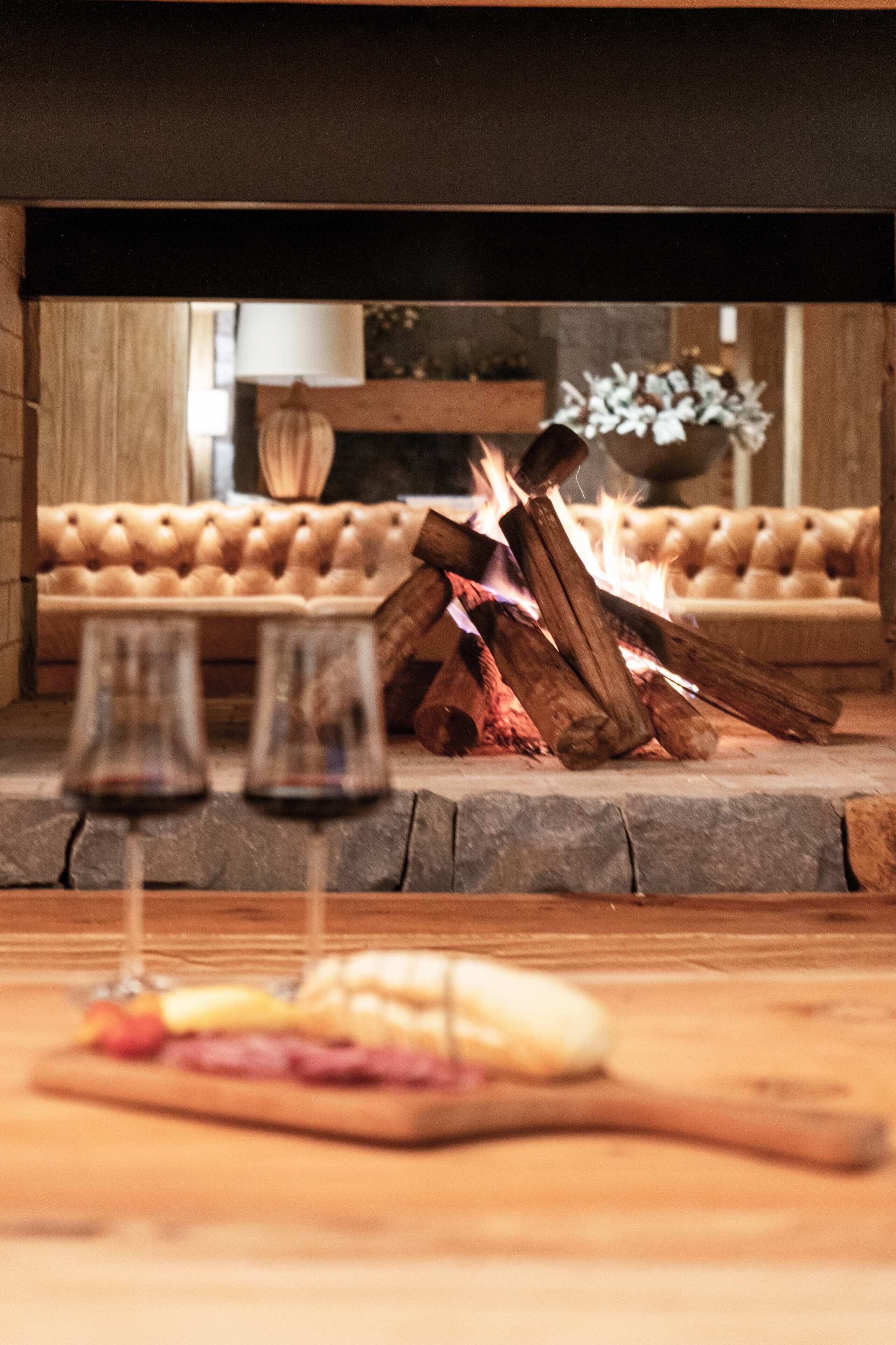 A cozy room with a fireplace, a sofa, and two glasses of red wine on a wooden table.