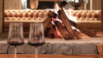 A cozy room with a fireplace, a sofa, and two glasses of red wine on a wooden table.