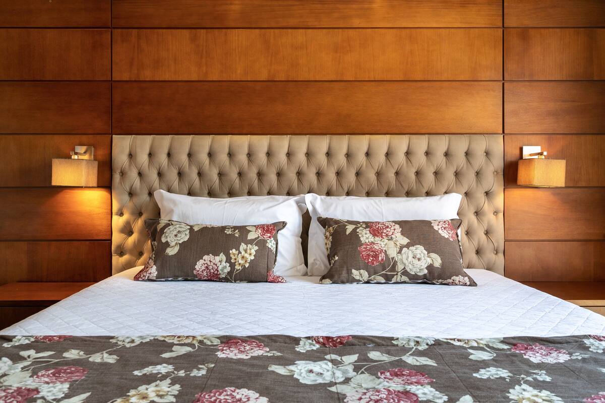 A neatly made bed with a floral bedspread, a tufted headboard, and two bedside lamps.