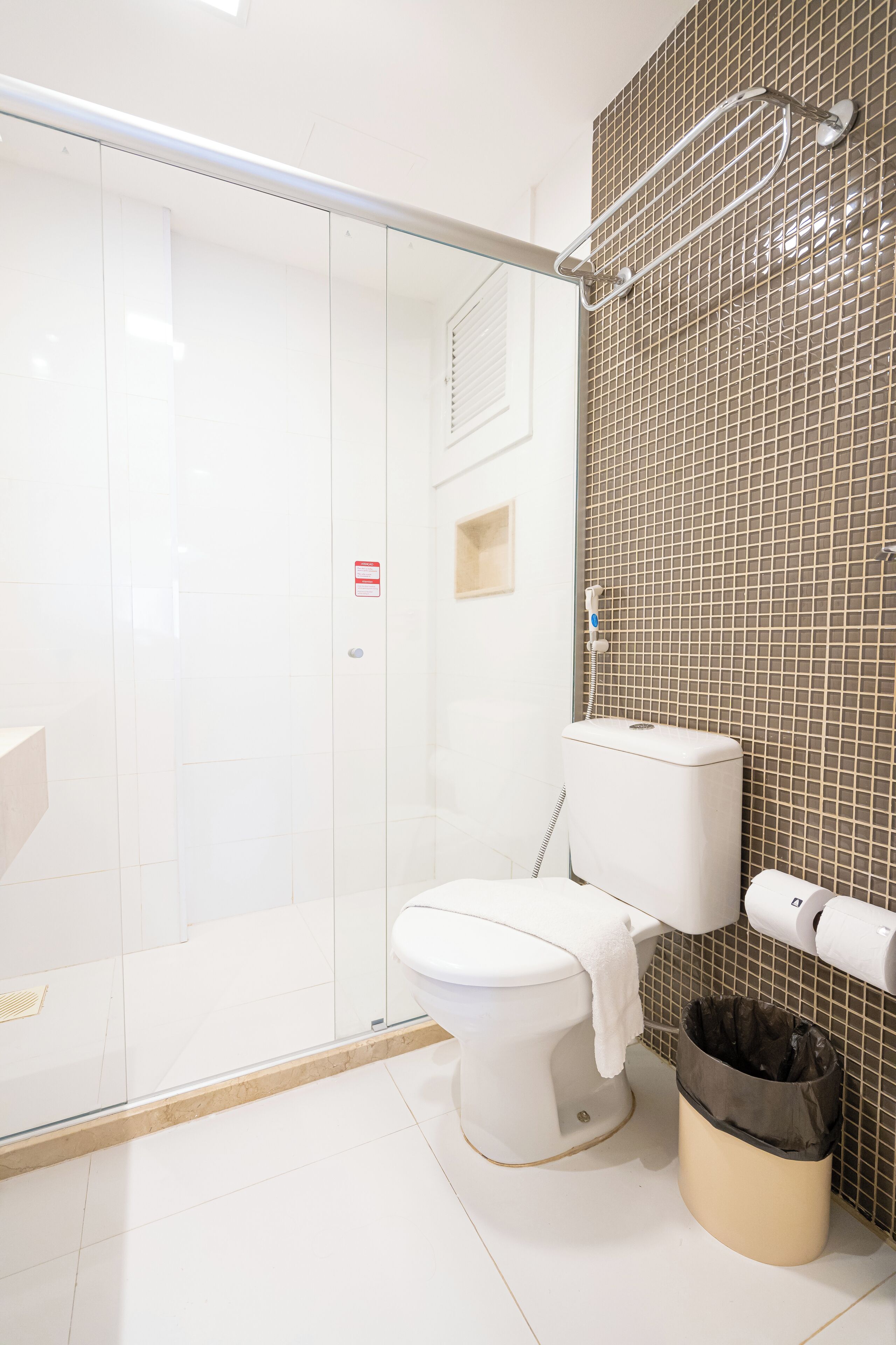 Un baño moderno con cabina de ducha de vidrio, inodoro y un cesto de basura.