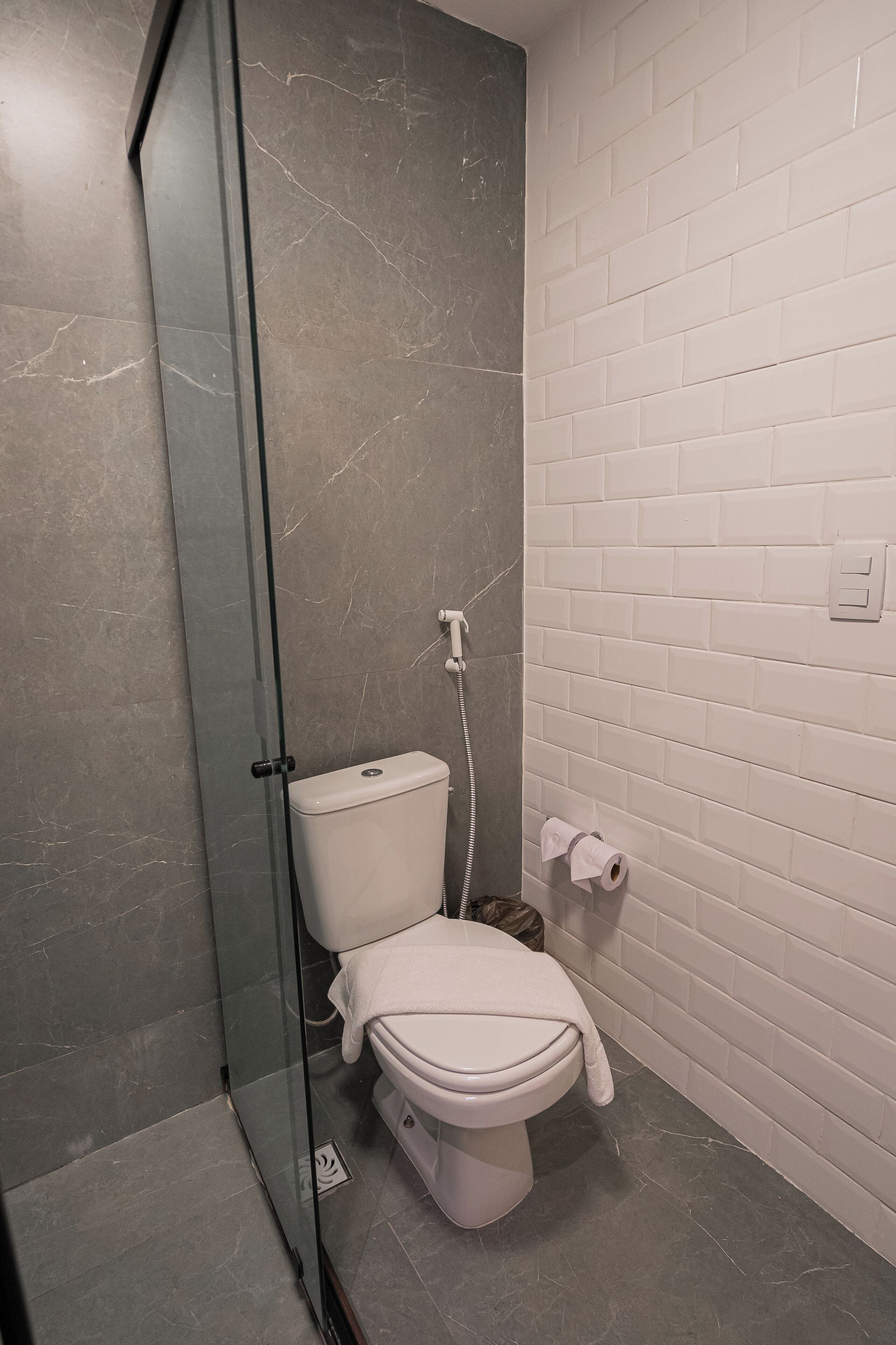 Un baño moderno con ducha de vidrio, inodoro blanco y pared de azulejos blancos.