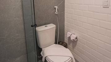 Un baño moderno con ducha de vidrio, inodoro blanco y pared de azulejos blancos.