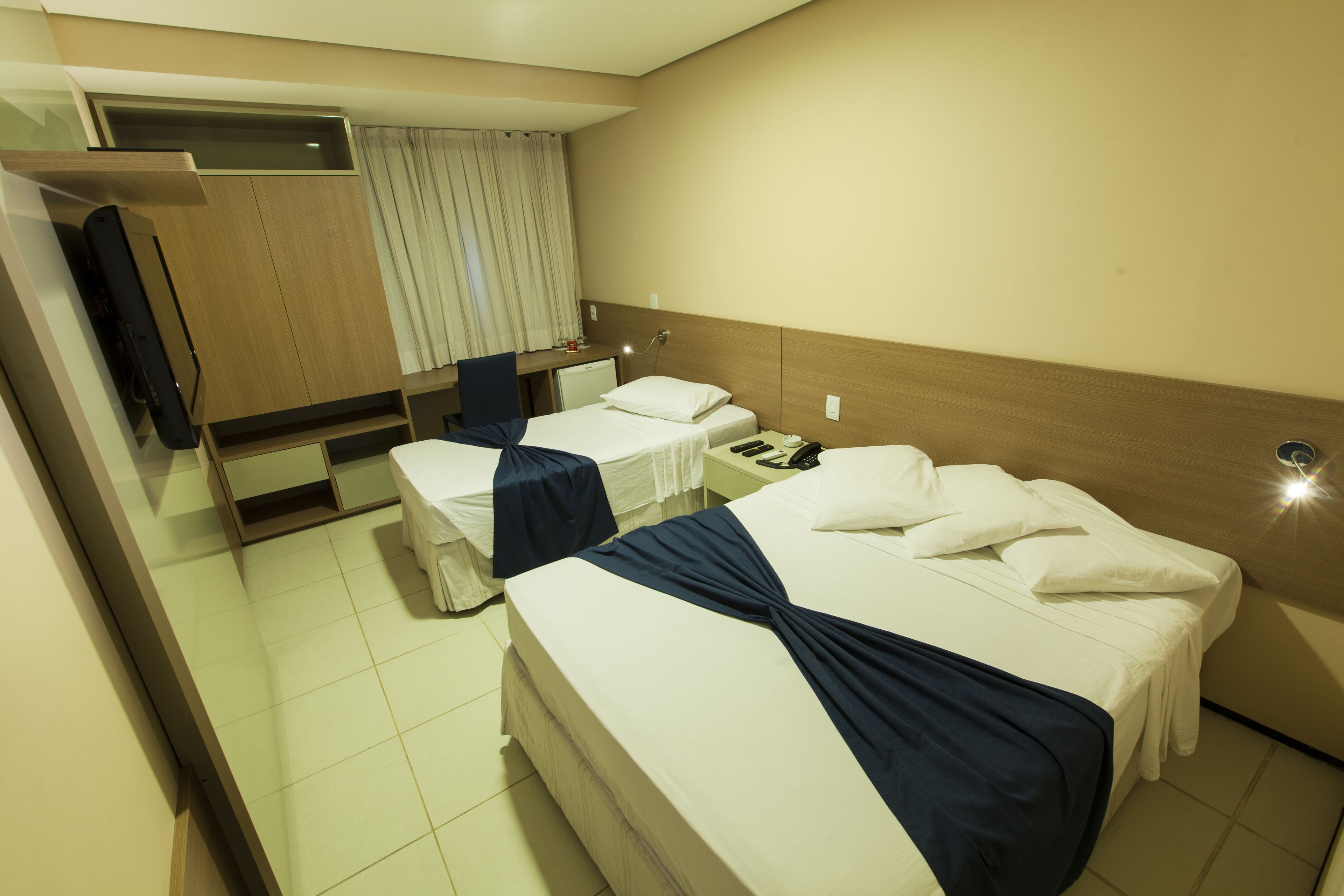 Habitación de hotel con dos camas individuales, un escritorio, una silla, un televisor y un espejo.