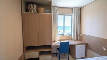A hotel room with a bed, a desk with a chair, a small refrigerator, and a wardrobe.