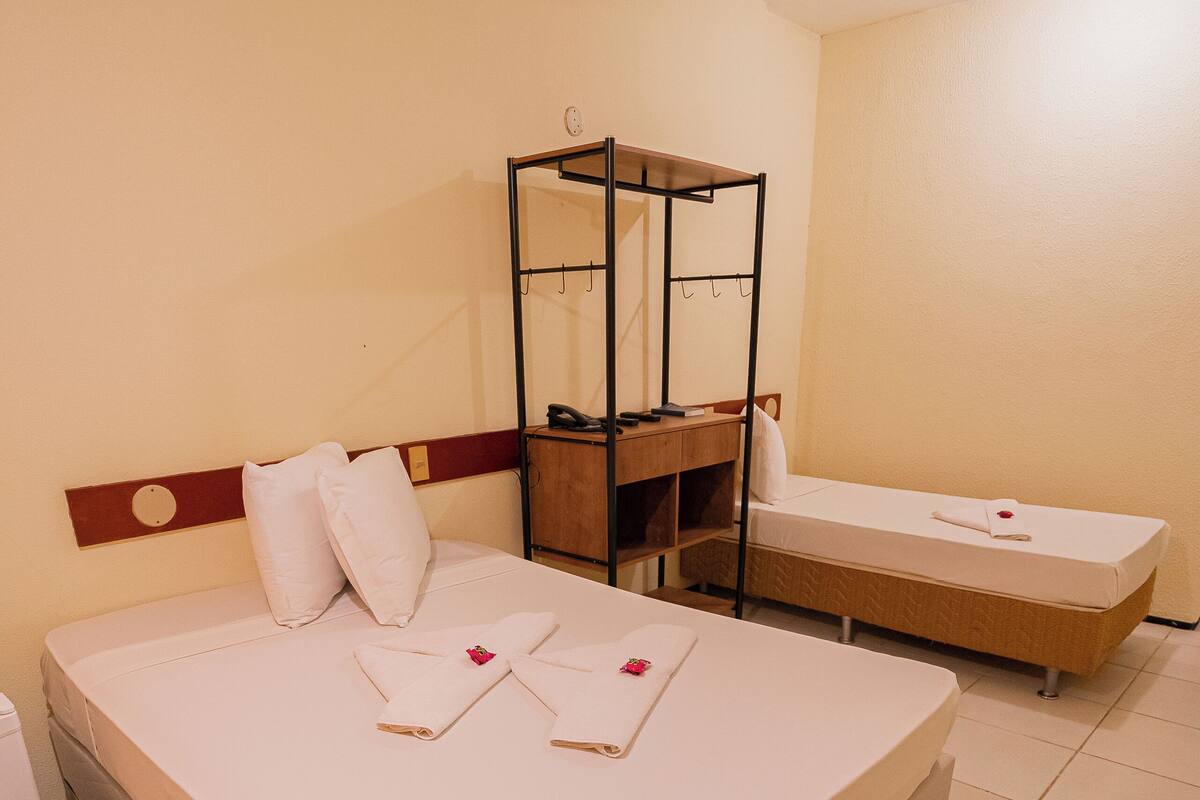 Ett hotellrum med en säng, ett litet skrivbord, en stol, ett sängbord och en spegel.