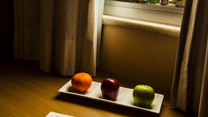 Una mesa con un plato, una servilleta, un tenedor y una bandeja con dos manzanas y una naranja.