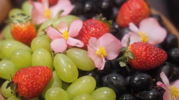 A wooden bowl filled with green grapes, strawberries, and blackberries, with pink flowers on top.