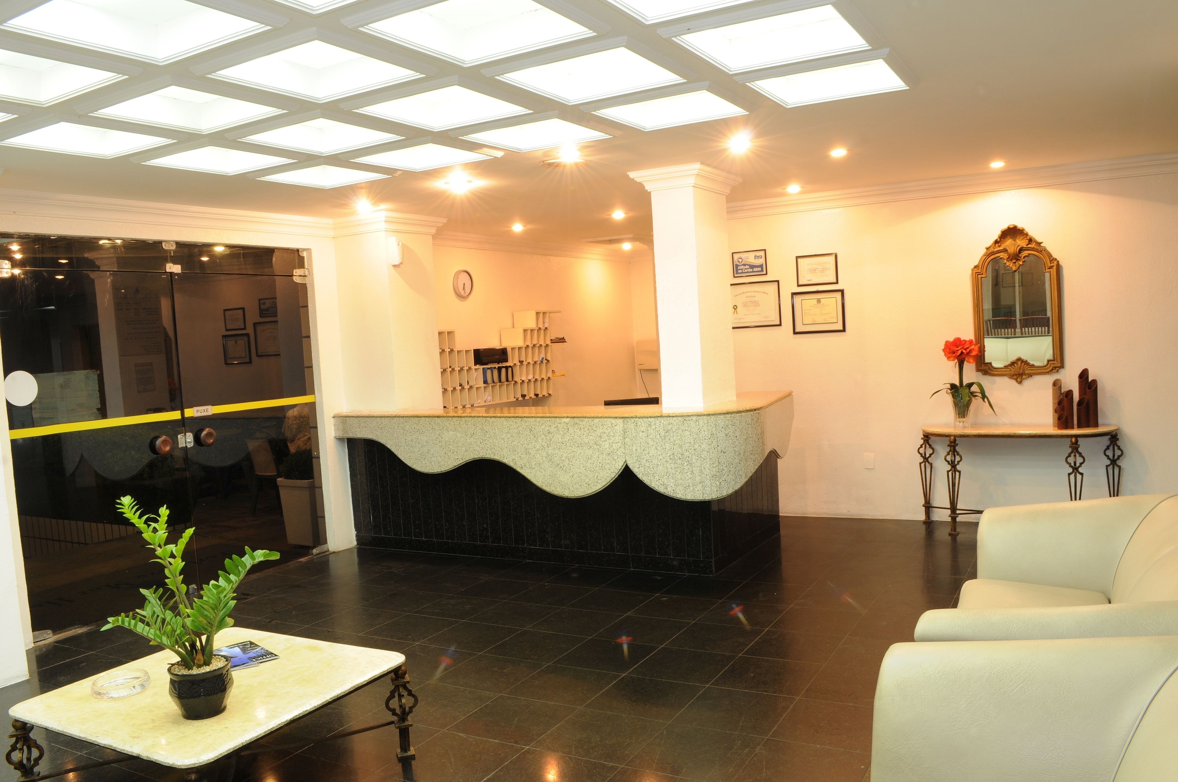 A reception area with a counter, a potted plant, a clock, framed certificates, and a mirror on the wall.