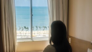 Una habitación de hotel con cama, ventana con cortinas y vista a la playa.