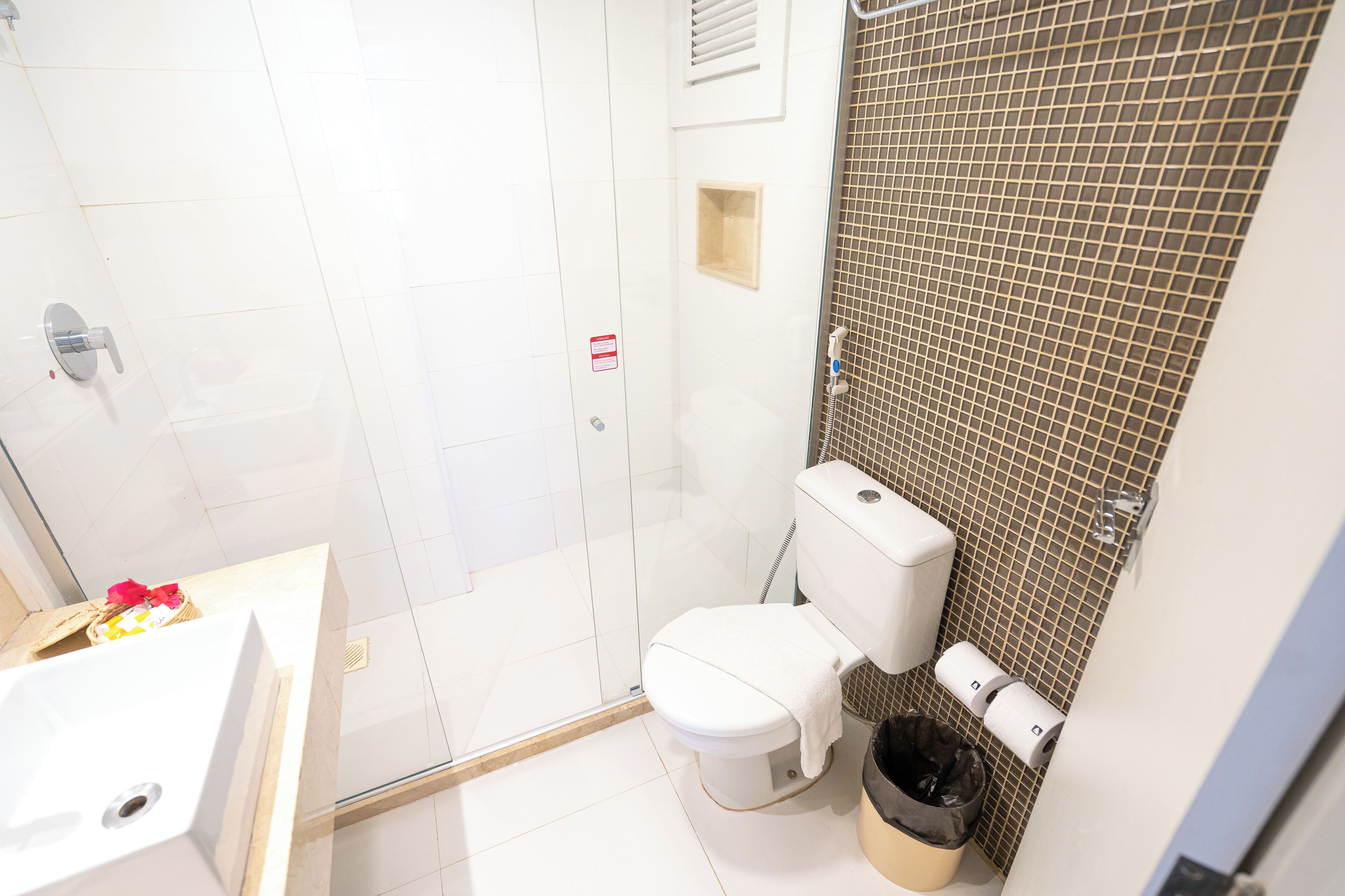 A bathroom with a shower, toilet, sink, and a trash bin.