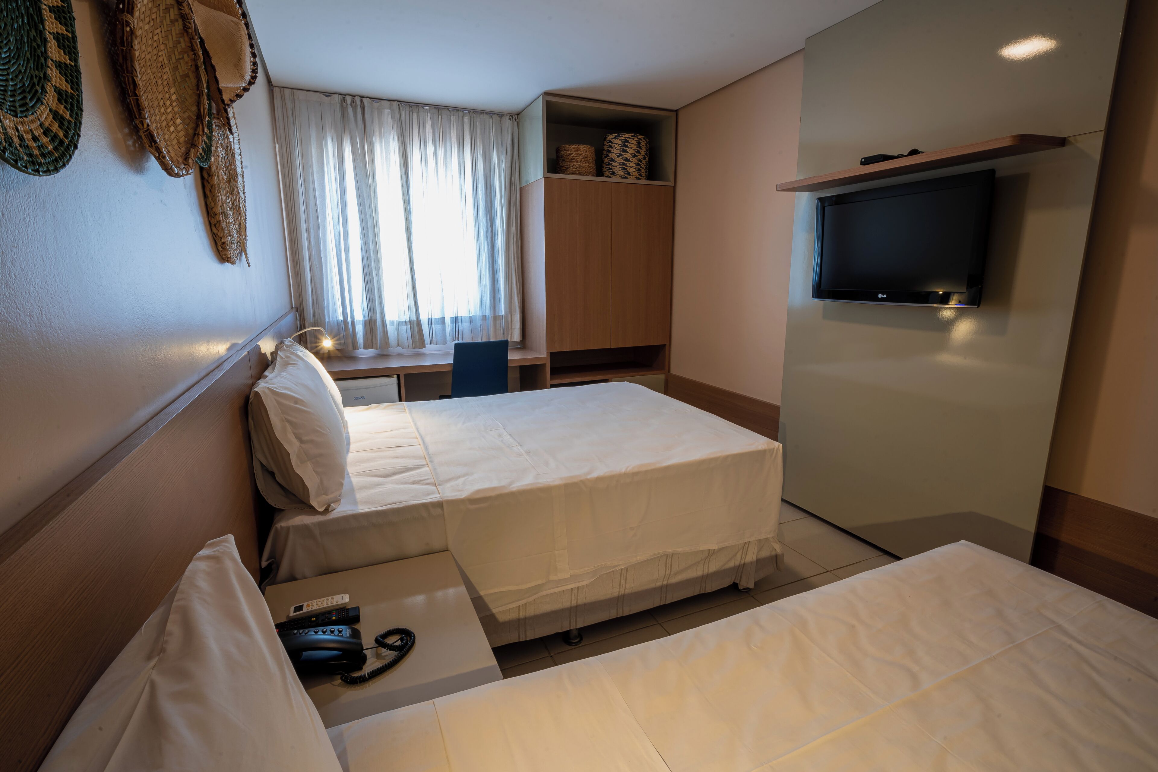 A hotel room with two beds, a TV, a desk, and a window with curtains.