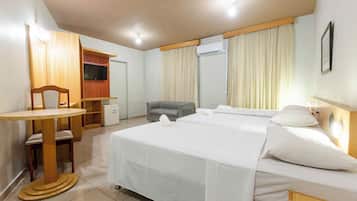Habitación de hotel con una cama grande, un escritorio con silla, un refrigerador pequeño, un equipo de aire acondicionado y un televisor en la pared.