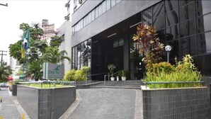 Un bâtiment moderne doté d’une grande entrée en verre, entouré d’espaces paysagers agrémentés de plantes et d’un chemin pavé menant à l’entrée.